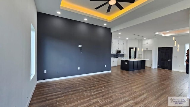 unfurnished living room featuring dark hardwood / wood-style floors, a raised ceiling, ceiling fan, and sink