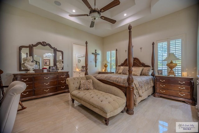 tiled bedroom featuring a towering ceiling, a tray ceiling, ensuite bath, and ceiling fan