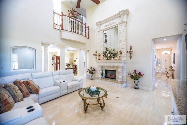 living room with ceiling fan, ornate columns, a fireplace, and a high ceiling