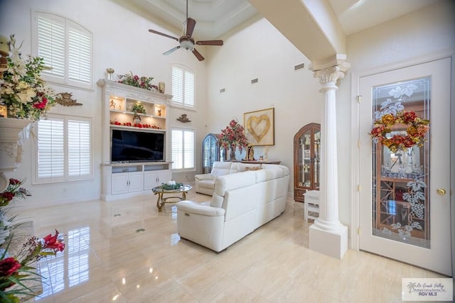 living room featuring ceiling fan, a towering ceiling, light tile patterned floors, and decorative columns