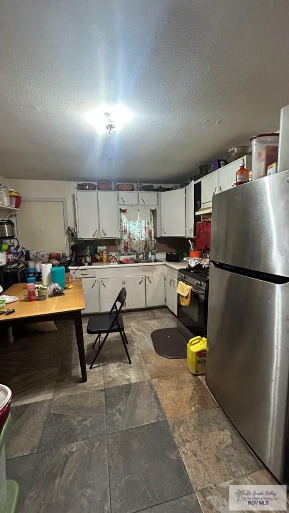 kitchen featuring black stove, white cabinetry, and stainless steel refrigerator