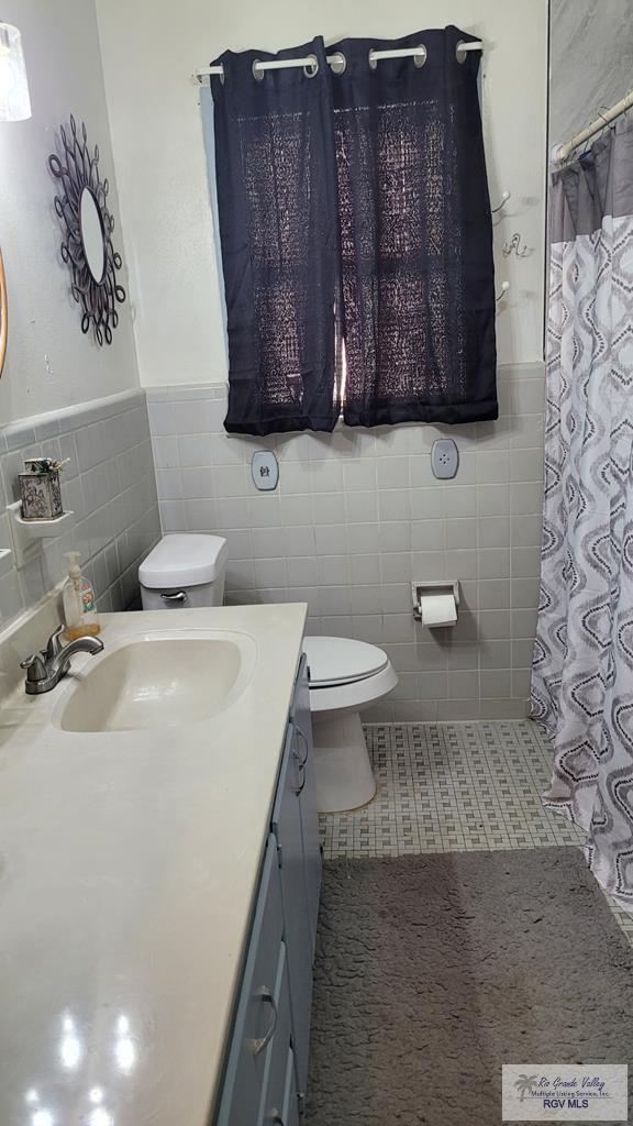 409 E Pine Ave Unit 0, La Feria, TX 78559 - bathroom with tile walls, toilet, vanity, a wainscoted wall, and curtained shower