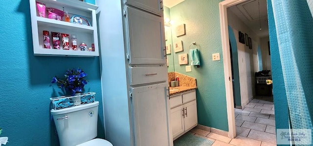 bathroom with vanity, toilet, a textured wall, and tile patterned floors