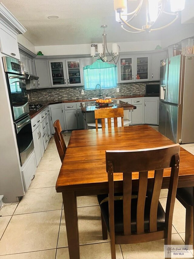 kitchen featuring appliances with stainless steel finishes, backsplash, gray cabinetry, pendant lighting, and a notable chandelier