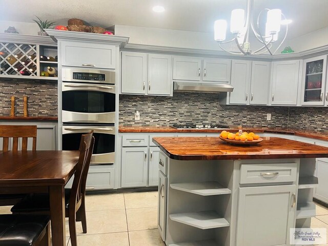 kitchen with double oven, butcher block counters, light tile patterned floors, and decorative light fixtures