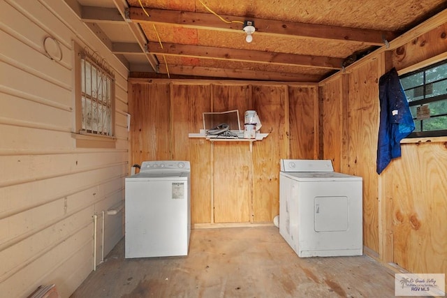 clothes washing area with washer and dryer, wooden walls, and laundry area