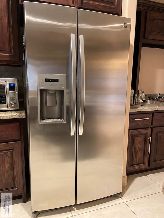 kitchen with dark brown cabinets, stainless steel fridge, and light tile patterned floors