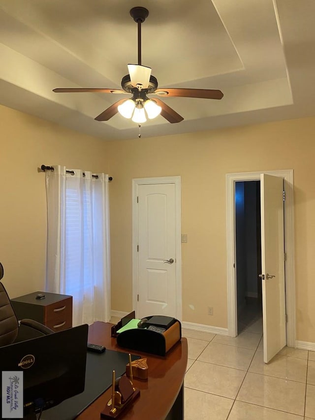 tiled home office with ceiling fan and a raised ceiling