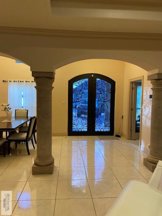 foyer with ornamental molding, light tile patterned flooring, ornate columns, and french doors