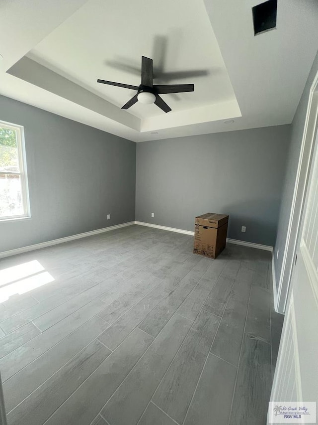 unfurnished bedroom with a raised ceiling, a ceiling fan, baseboards, and dark wood-type flooring