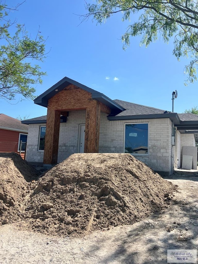 view of front of house featuring brick siding and roof with shingles