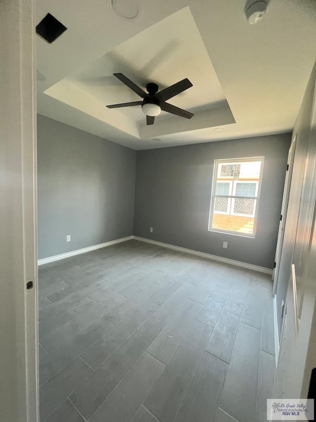 spare room featuring a tray ceiling, wood finished floors, baseboards, and ceiling fan