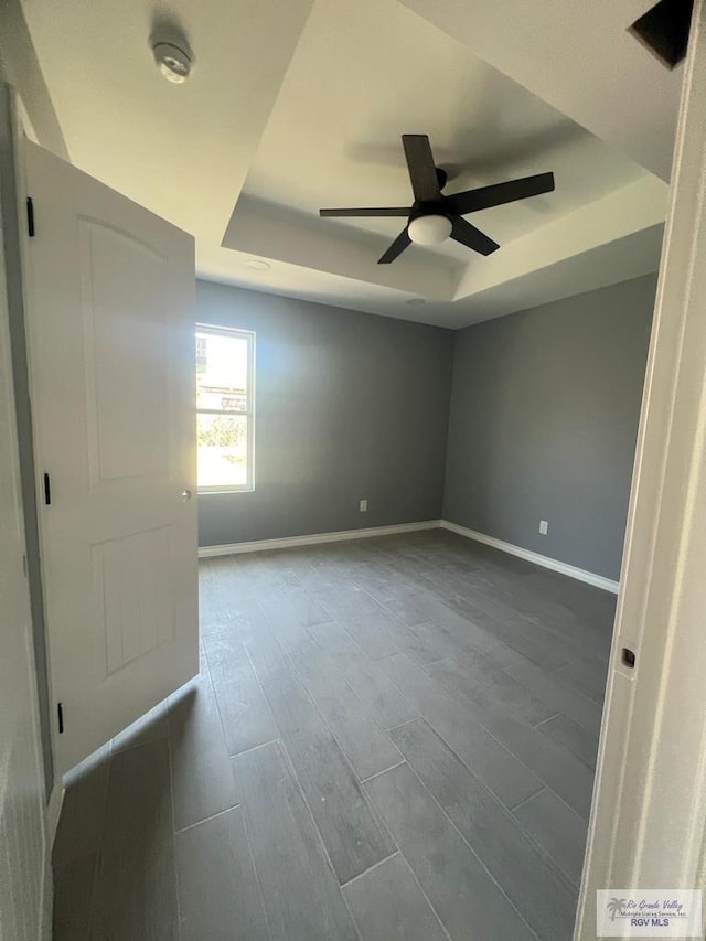 empty room featuring a tray ceiling, baseboards, ceiling fan, and wood tiled floor