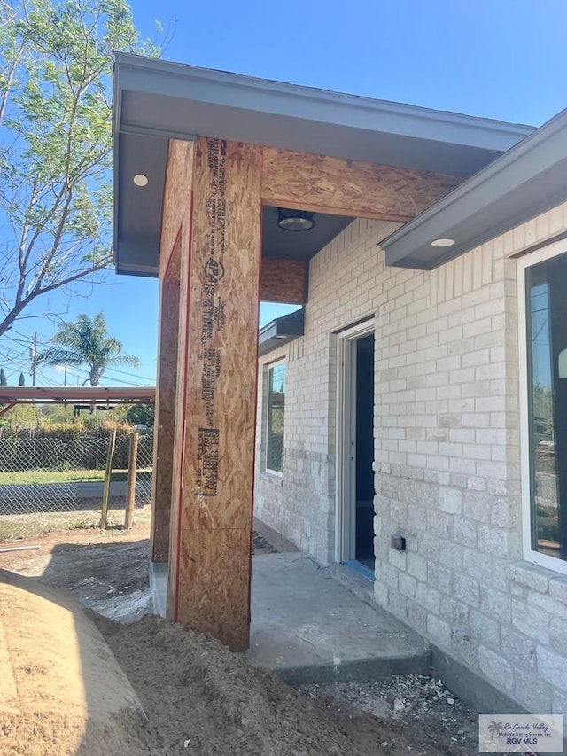 view of exterior entry featuring brick siding and fence