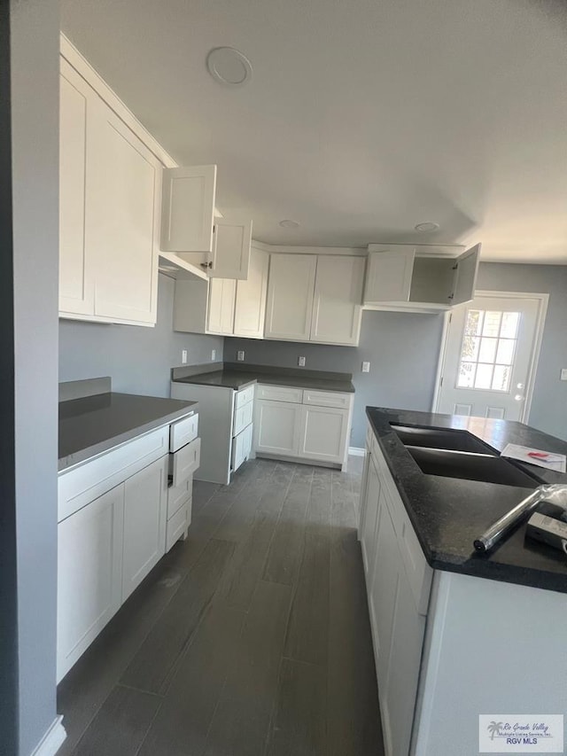 kitchen with a kitchen island, dark wood finished floors, a sink, white cabinetry, and dark countertops