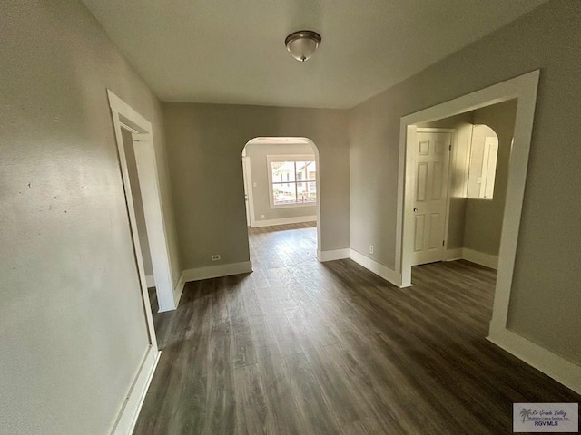 interior space with baseboards, arched walkways, and dark wood-type flooring