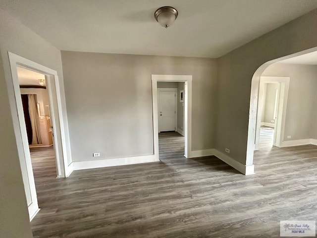 empty room featuring dark wood finished floors, baseboards, and arched walkways
