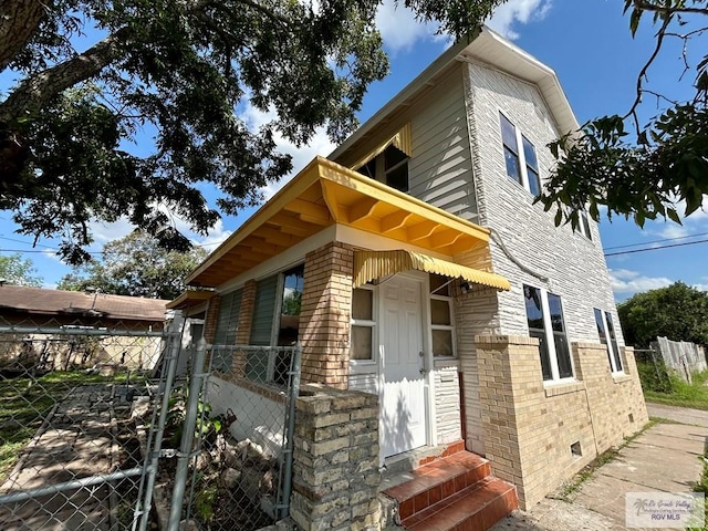 view of front of home with brick siding, crawl space, fence, and entry steps