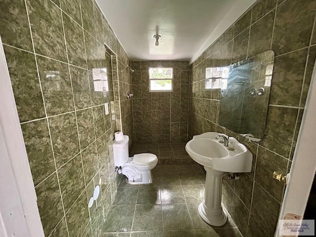 bathroom featuring tile patterned floors, toilet, tile walls, and a tile shower