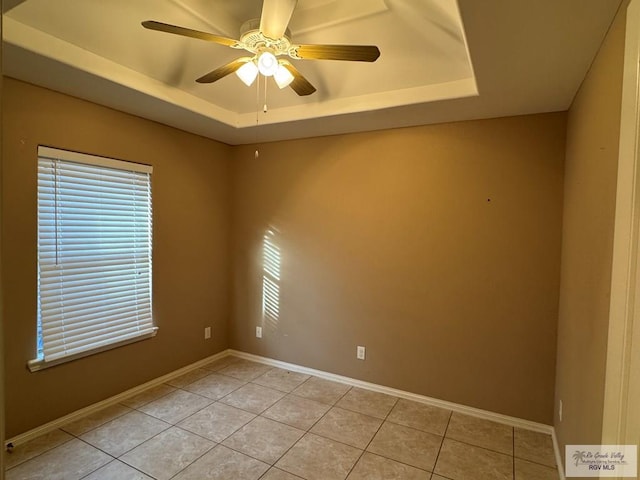 tiled empty room with ceiling fan and a tray ceiling