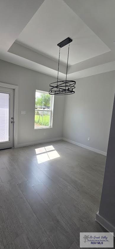 unfurnished dining area with a raised ceiling, dark hardwood / wood-style flooring, and a notable chandelier