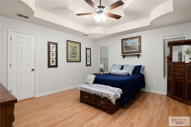 bedroom with ceiling fan, light hardwood / wood-style floors, and a raised ceiling