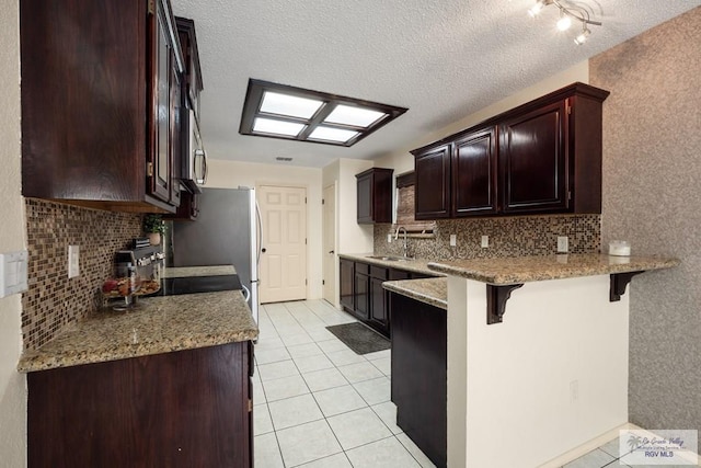5 Mantua St, Brownsville, TX 78526 - kitchen featuring a breakfast bar, backsplash, a peninsula, light tile patterned floors, and a textured ceiling