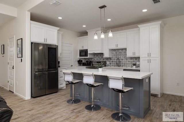3214 W Hapner St, Harlingen, TX 78550 - kitchen featuring appliances with stainless steel finishes, white cabinets, light wood-style floors, tasteful backsplash, and light countertops