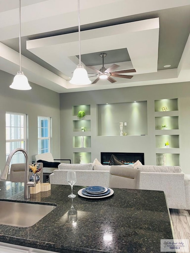 kitchen featuring dark stone counters, sink, hanging light fixtures, built in features, and a tray ceiling