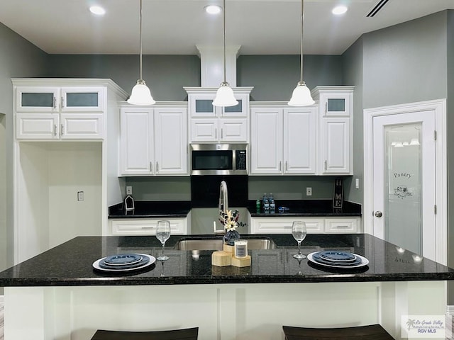 kitchen featuring pendant lighting, white cabinets, and an island with sink