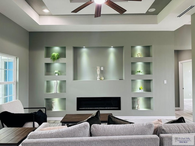 living room featuring a tray ceiling, built in features, ceiling fan, and light hardwood / wood-style flooring