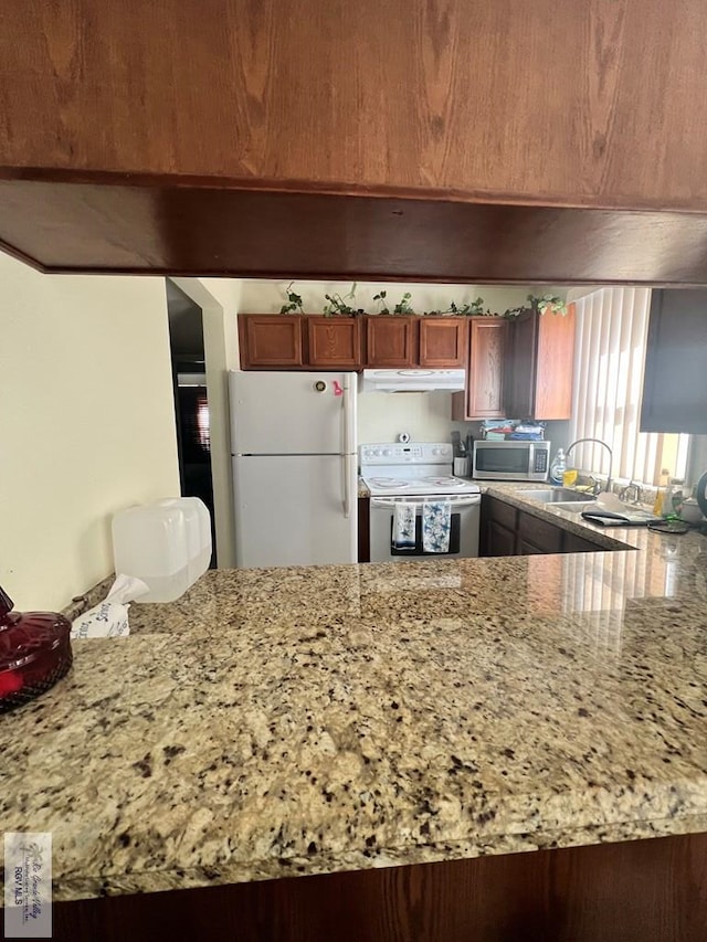 kitchen with kitchen peninsula, light stone countertops, white appliances, and sink