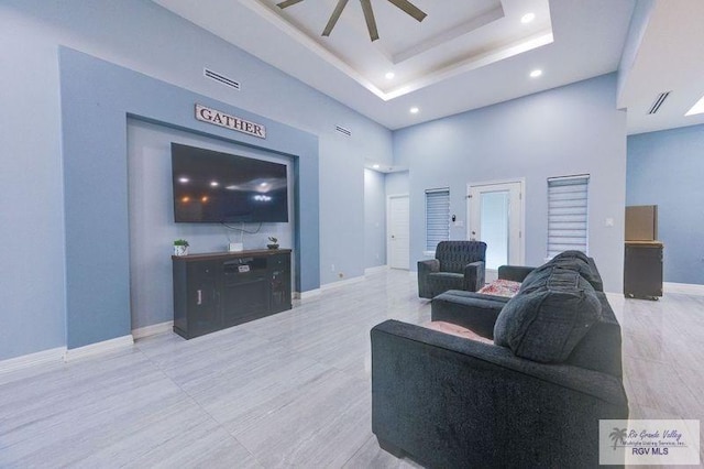 living area with a tray ceiling, baseboards, recessed lighting, a ceiling fan, and a high ceiling