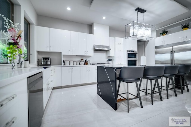 kitchen with white cabinets, appliances with stainless steel finishes, decorative light fixtures, a kitchen island, and a breakfast bar area