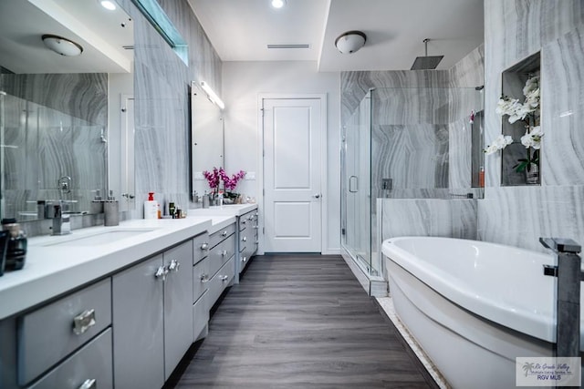 bathroom featuring plus walk in shower, hardwood / wood-style floors, vanity, and tile walls