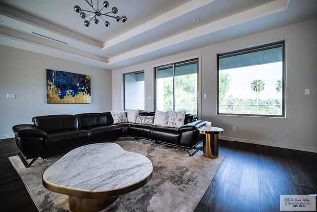 living room featuring a raised ceiling, dark hardwood / wood-style flooring, and a notable chandelier