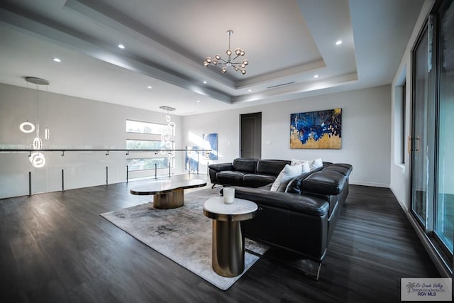 living room featuring a tray ceiling, dark hardwood / wood-style flooring, and a notable chandelier