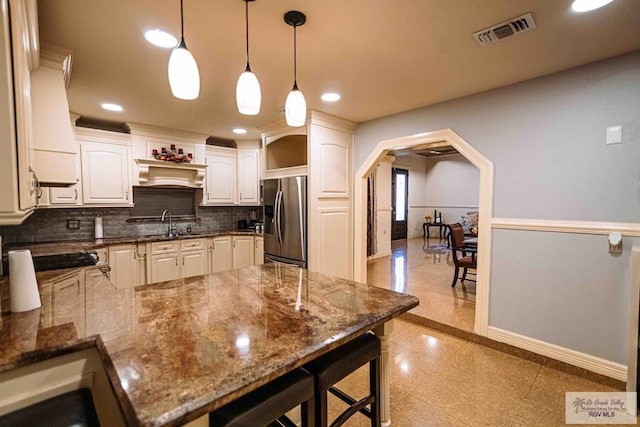 kitchen with dark stone countertops, a breakfast bar, pendant lighting, stainless steel refrigerator with ice dispenser, and backsplash