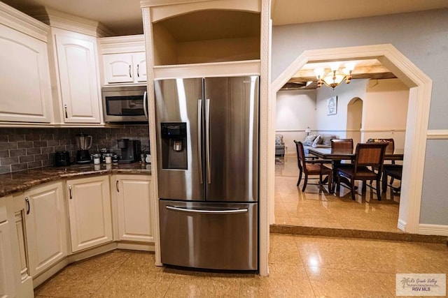 kitchen with a chandelier, stainless steel appliances, tasteful backsplash, white cabinets, and dark stone counters