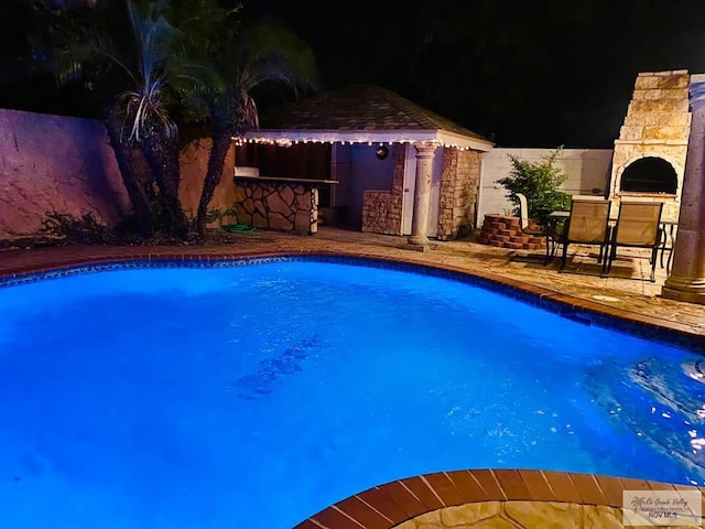 pool at night with an outdoor bar, a patio area, and an outdoor fireplace