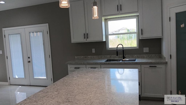 kitchen with french doors, white cabinets, sink, hanging light fixtures, and light tile patterned floors