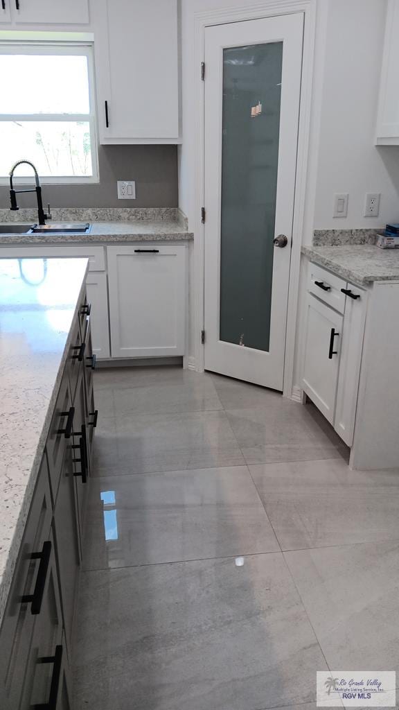 kitchen featuring light stone counters, sink, and white cabinets