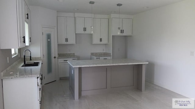 kitchen with light stone counters, a kitchen island, sink, decorative light fixtures, and white cabinetry