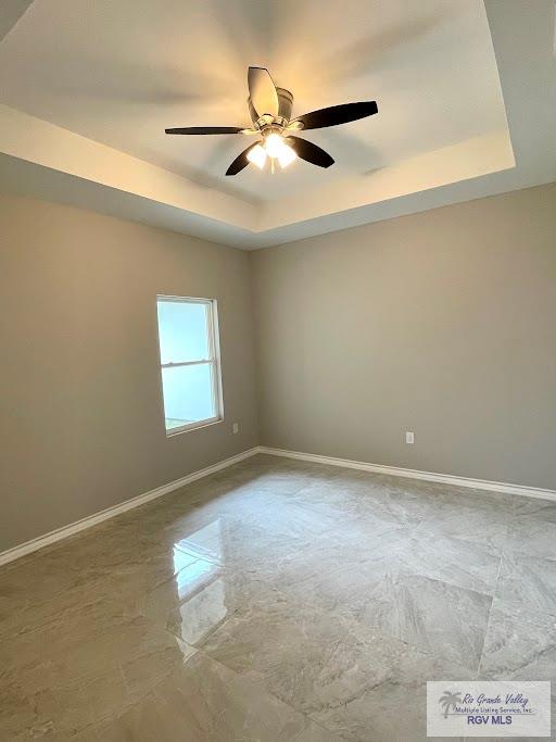 empty room featuring a tray ceiling and ceiling fan