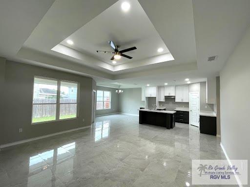 kitchen with a raised ceiling, ceiling fan, a center island, and white cabinets