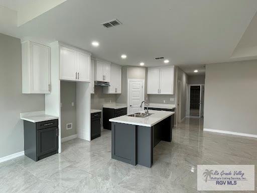 kitchen with decorative backsplash, a center island with sink, white cabinets, and sink