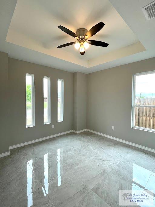 spare room with ceiling fan, a healthy amount of sunlight, and a tray ceiling