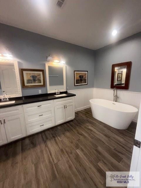 201 Terrace Ln, Harlingen, TX 78550 - bathroom featuring double vanity, a soaking tub, a wainscoted wall, and wood finished floors