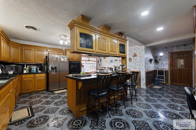 kitchen with glass insert cabinets, brown cabinetry, stainless steel fridge, dark countertops, and a textured ceiling