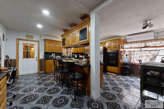 kitchen with dobule oven black, a wall mounted air conditioner, dark countertops, and a textured ceiling
